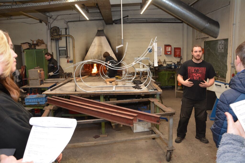 Ein Auszubildender aus der Metallwerkstatt steht neben einem Tisch mit einem Metallgerüst